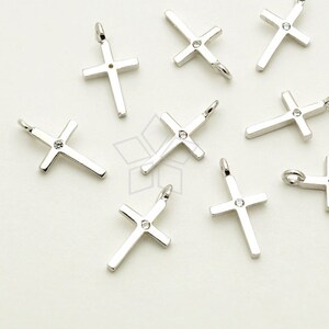 May include: A group of silver cross charms with a single clear rhinestone in the center of each cross.