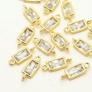 May include: A group of gold-toned rectangular crystal charms with a loop on each end. The charms are scattered on a white surface.