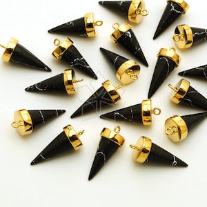 Peut inclure: Une collection de pendentifs en forme de cône noir et or avec un motif marbré. Les pendentifs ont une boucle dorée en haut pour les attacher à des bijoux.