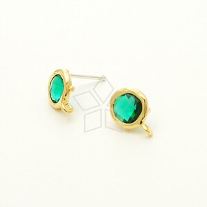 May include: A pair of gold-tone earrings with green gemstone accents. Each earring features a round, faceted gemstone set in a textured gold-tone setting. The earrings have a small loop on the bottom for attaching to a chain or other jewelry.