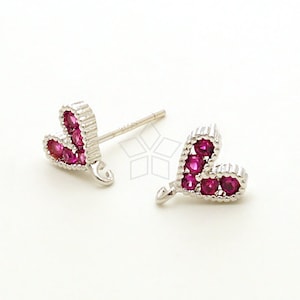 Può includere: Un paio di orecchini a bottone color argento a forma di cuore. Ogni cuore è impreziosito da piccole gemme rosa brillante e rotonde. Gli orecchini sono su uno sfondo bianco, evidenziando il loro design e colore.