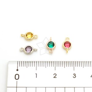 May include: Four colorful gemstone connectors with gold and silver-tone settings. The gemstones are yellow, purple, green, and red. Each connector has a loop on either side for attaching to other jewelry components. A ruler is in the foreground.