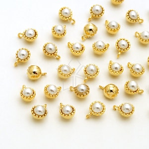 May include: A collection of gold-toned pearl charms with a loop for attaching to jewelry. The charms are scattered on a white surface.