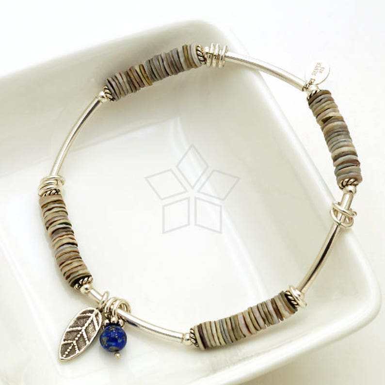 May include: Silver bracelet with a blue gemstone charm and a leaf charm. The bracelet is made of silver and has a series of small, round, grey and white beads.