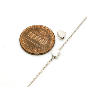 May include: A silver chain necklace with two small heart-shaped charms. The necklace is shown next to a US penny for size comparison.