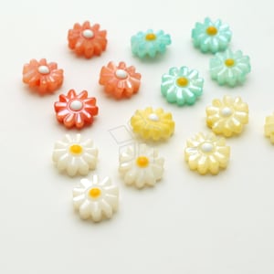 May include: Assortment of colorful flower-shaped buttons in various shades of blue, yellow, and orange. The buttons have a pearly finish and a raised center.
