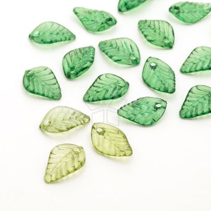 Può includere: Una collezione di perline traslucide a forma di foglia verde, con un foro nella parte superiore per l'infilatura. Le perline presentano dettagliate venature e variano leggermente di tonalità, alcune appaiono più chiare.