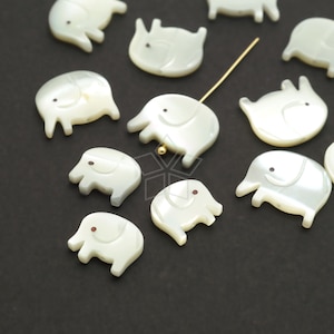 Puede incluir: Una colección de encantos de elefante de madreperla blanca con ojos marrones. Los encantos están esparcidos sobre una superficie negra.