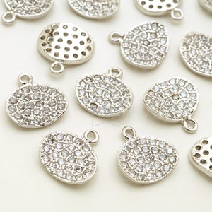May include: Silver tone metal charms with a round shape and a pave setting of clear rhinestones. The charms have two jump rings for attaching to jewelry.