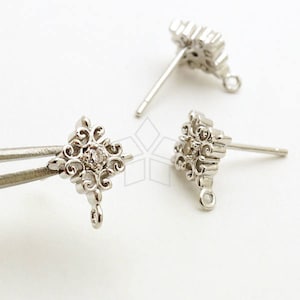 Puede incluir: Un par de cierres de pendientes de plata con un strass transparente en el centro de cada uno. Los cierres tienen un diseño decorativo y ornamentado.