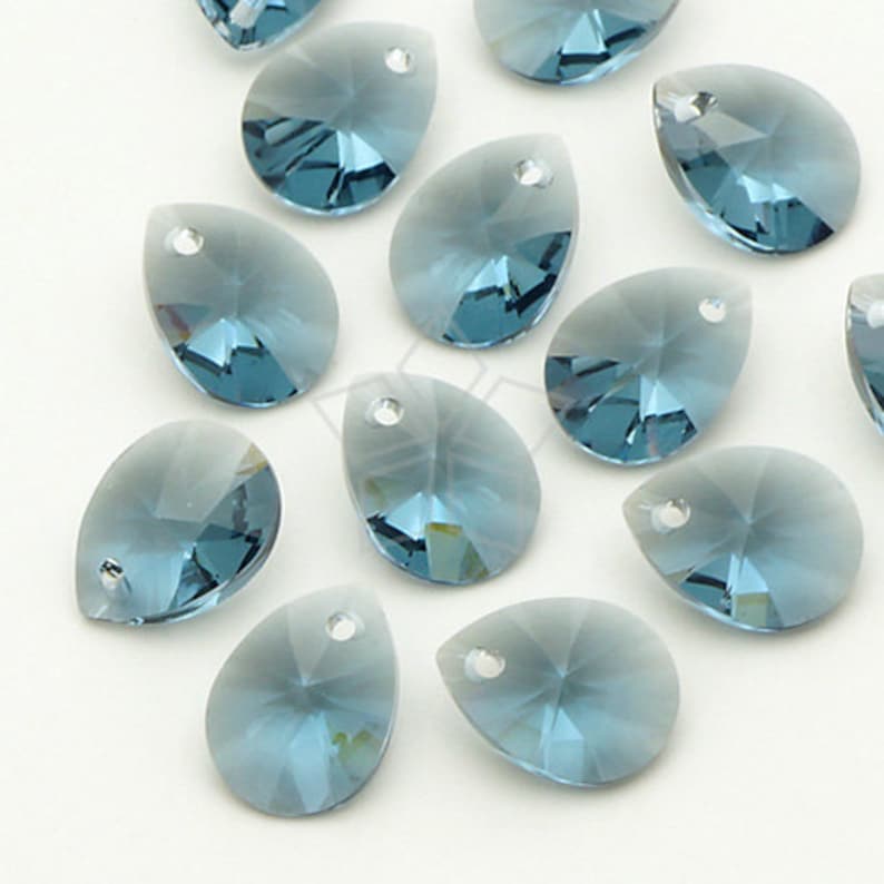 May include: Close-up of several teardrop-shaped, faceted blue crystal beads. Each bead has a small hole at the top for stringing. The crystals have a gradient effect, transitioning from a lighter blue to a deeper shade.