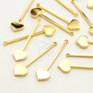 May include: Gold-toned metal heart-shaped charms with a straight metal bar attached to the top of each heart. The charms are scattered on a white surface.
