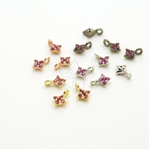 Puede incluir: Surtido de pequeños amuletos de forma cuadrada con detalles de piedras preciosas rojas. Los amuletos están hechos de diferentes metales, incluyendo oro, plata y bronce.