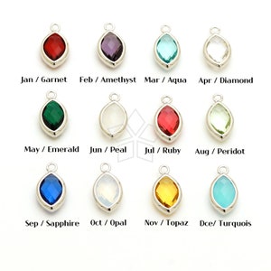May include: Twelve gemstone charms in a silver setting, each representing a different month of the year. The charms are arranged in four rows of three, with the month and gemstone name listed below each charm.