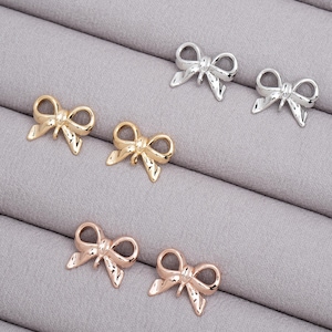 May include: Five gold, silver, and rose gold bow charms. The charms are in the shape of a bow with a loop at the top for attaching to a necklace, bracelet, or other jewelry.