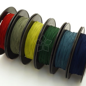 May include: Six spools of thread in different colours: red, green, yellow, dark green, blue, and navy blue. The spools are arranged in a row, with the red spool on the left and the navy blue spool on the right.