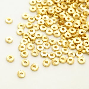 Puede incluir: Una gran cantidad de anillos de salto de metal de color dorado. Los anillos están dispersos sobre una superficie blanca.