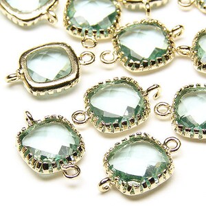 Può includere: Primo piano di diverse perline di vetro quadrato verde chiaro con montature in metallo color oro. Ogni perlina ha un anello su due lati per l'infilatura. Le perline sono sfaccettate e riflettenti, ideali per la creazione di gioielli.