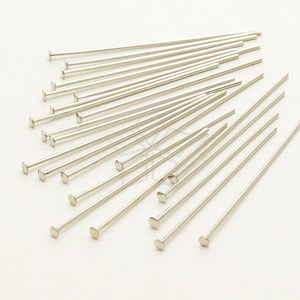 Puede incluir: Primer plano de un montón de alfileres de cabeza plateada. Los alfileres miden aproximadamente 5 cm de largo y tienen una cabeza plana.