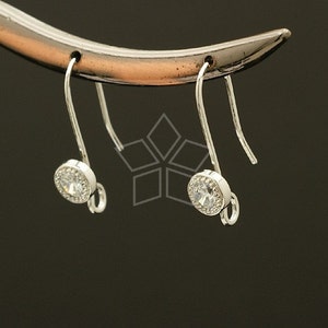 May include: A pair of silver earrings with clear crystal stones set in a round bezel setting. The earrings have a hook closure.