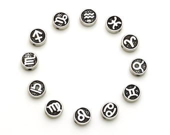 May include: Twelve silver-toned zodiac charms with black enamel and white astrological symbols arranged in a circle on a white background.