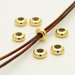 May include: Gold-toned metal beads with a clear center, strung on a brown leather cord. The beads are round and have a slightly domed shape.