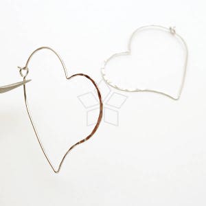 May include: A pair of silver heart-shaped hoop earrings. The earrings are made of thin wire and have a hammered texture.