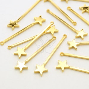 Puede incluir: Encantos de estrella de metal dorado con una barra larga, delgada y recta unida a la parte posterior de cada estrella. Los encantos están dispersos sobre una superficie blanca.