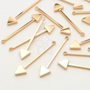 May include: A group of gold-colored arrow-shaped charms with a loop at the top. The charms are arranged in a random pattern on a white surface.