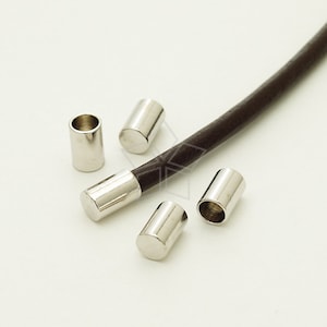 May include: Five silver metal cord end caps for leather cord. The cord end caps are cylindrical and have a smooth, shiny finish.