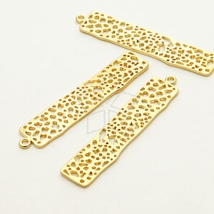 Può includere: Tre ciondoli a barra in metallo color oro con un motivo delicato, intricato e ripetitivo di piccoli cerchi e ovali. I ciondoli hanno una finitura liscia e lucida e sono perfetti per aggiungere un tocco di eleganza ai progetti di gioielleria.