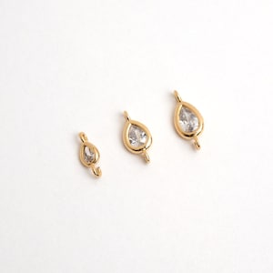 Puede incluir: Tres colgantes dorados en forma de lágrima con piedras claras y facetadas. Cada colgante tiene un pequeño lazo en la parte superior e inferior para sujetarlo a una cadena u otro componente de joyería. Los colgantes se muestran sobre un fondo blanco.
