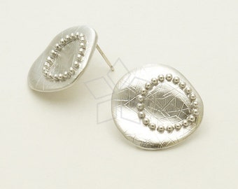 May include: A pair of silver-toned stud earrings. Each earring has an irregular, organic shape with a textured surface. A circle of small, raised beads is set within the center of each earring. The earrings are displayed on a white background.