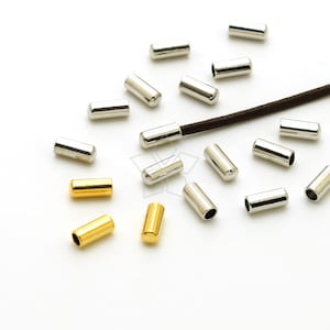 Puede incluir: Una colección de terminales de cordón de metal plateado y dorado. Los terminales de cordón están esparcidos sobre una superficie blanca.