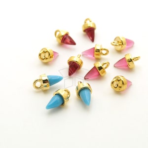 May include: Assortment of gold-toned metal charms with pointed glass tips. Some charms are pink and some are blue.