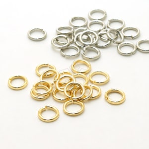 Puede incluir: Un montón de anillos de salto dorados y un montón de anillos de salto plateados. Los anillos de salto son pequeños y redondos.