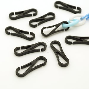 May include: A collection of black plastic spring clips, some of which are attached to a chain of white and light blue plastic links. The clips are open and ready to be attached to something. The background is white.