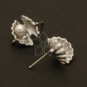 Puede incluir: Un par de pendientes de plata con un diseño de concha que contiene una perla. Los pendientes son de metal y tienen un cierre de poste.