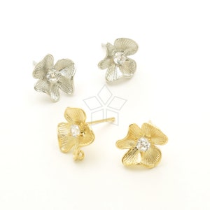May include: Four flower-shaped stud earrings. Two are silver-colored, and two are gold-colored. Each earring features a clear, round gemstone in the center. The earrings are set against a white background.