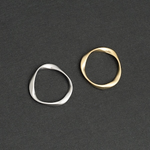 Könnte beinhalten: Zwei schlichte, moderne Ringe, einer in Silber und einer in Gold, auf schwarzem Hintergrund. Die Ringe sind beide oval geformt mit einer leicht unregelmäßigen, organischen Form.