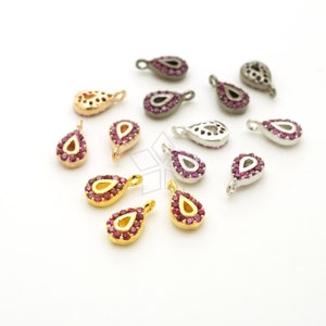 May include: Assortment of teardrop-shaped charms with a decorative border of small pink rhinestones. The charms are made of different metals, including gold, silver, and black.