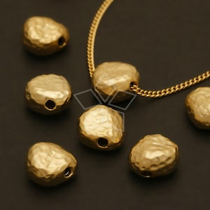 May include: A gold chain necklace with a hammered gold pendant. The pendant is shaped like a small, irregular oval. There are six additional hammered gold pendants scattered around the necklace.