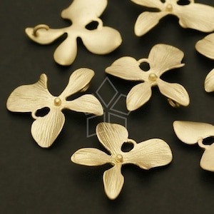 Puede incluir: Primer plano de varios componentes de joyería en forma de flor de color oro mate. Cada componente tiene cuatro pétalos y un pequeño agujero. Los componentes son probablemente para la fabricación de joyas, como pendientes o colgantes.