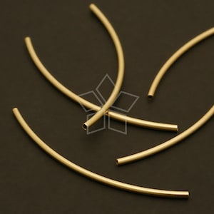 Puede incluir: Cuatro aros de metal de color dorado, cada uno con una curva ligeramente diferente, están dispuestos sobre una superficie negra.