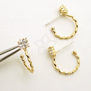 May include: A pair of gold hoop earrings with a clear square-shaped crystal on each earring. The earrings have a twisted design and are made of metal.
