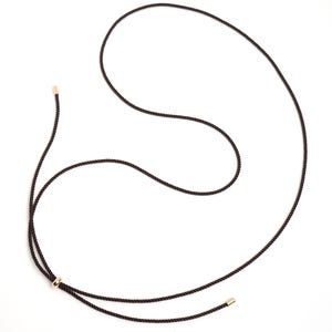 Può includere: Una collana in corda marrone scuro con dettagli metallici color oro. La collana presenta un nodo scorrevole e terminali dorati alle estremità della corda, creando un design minimalista ed elegante. La collana è esposta su sfondo bianco.
