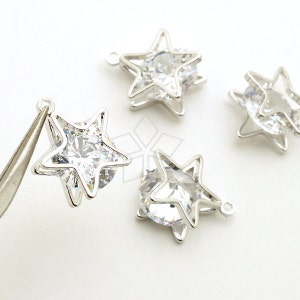 Pode incluir: Quatro pingentes de estrela prateados com pedras de cristal transparentes no centro. Cada pingente tem um laço para prender em joias ou outras manualidades.