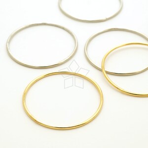May include: Four metal hoops, two silver and two gold, arranged on a white surface. The hoops are different sizes.