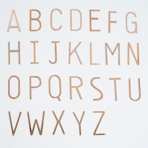May include: A set of 26 gold-colored metal letters, from A to Z, arranged in alphabetical order. Each letter is individually cut out and has a slightly raised edge.
