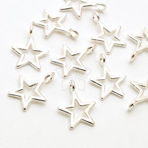May include: A collection of silver-colored star charms with a loop at the top for hanging. The charms are open in the center, creating a star shape. The charms are scattered on a white surface.